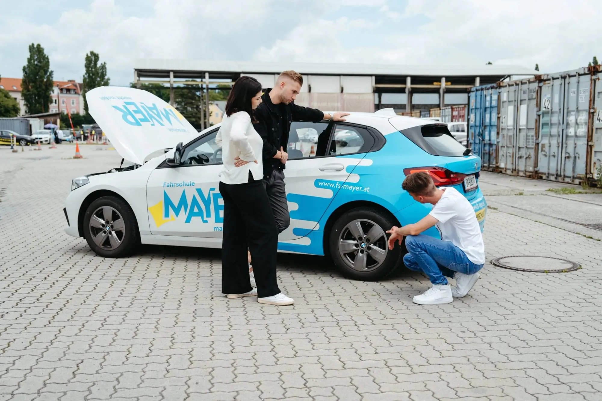 Zwei Fahrschüler:innen am Übungsplatz neben einem Fahrschulauto der Fahrschule Mayer